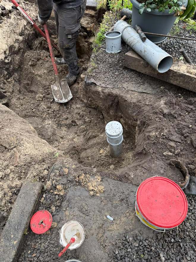 Graafwerk naast een woning waarbij een ontstoppingsstuk met dop uit de grond steekt.