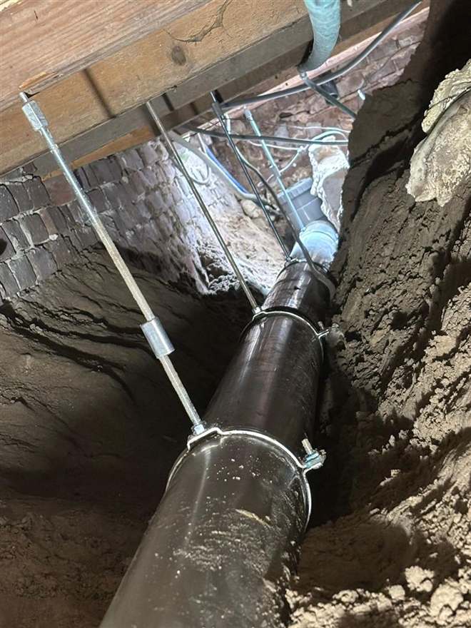 Nieuwe rioolleiding opgehangen aan draadstangen in een kruipruimte onder een woning.