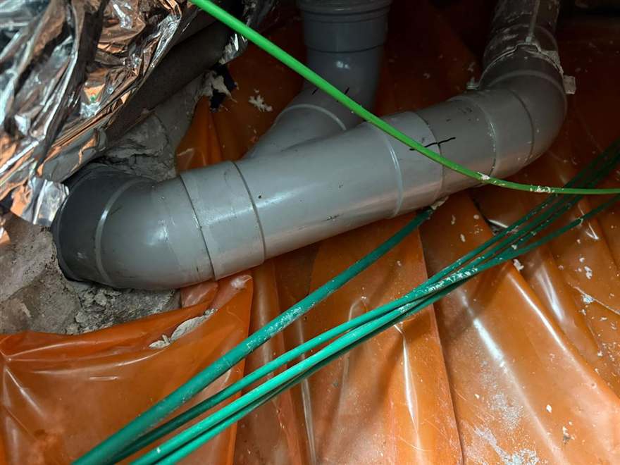 Nieuw aangelegde grijze PVC-afvoer met T-stuk onder de vloer, op oranje folie.
